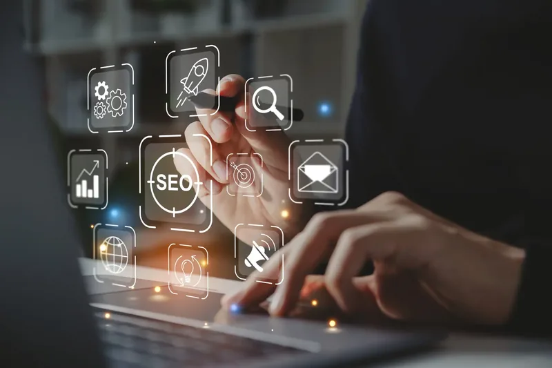 Mains sur le clavier d'un ordinateur portable, avec des icônes SEO lumineuses en surimpression