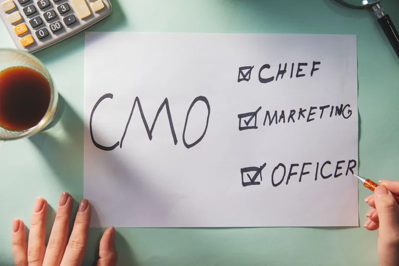 Feuille où sont écrits à la main « CMO » et « Chief Marketing Officer », à côté d'une calculatrice et d'un café