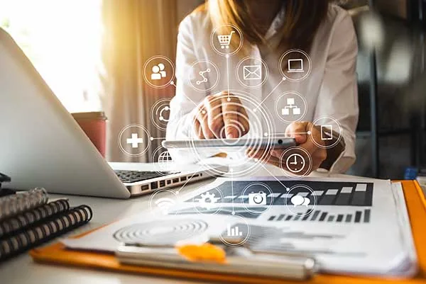Personne travaillant sur une tablette et un ordinateur portable, entourée d'icônes numériques
